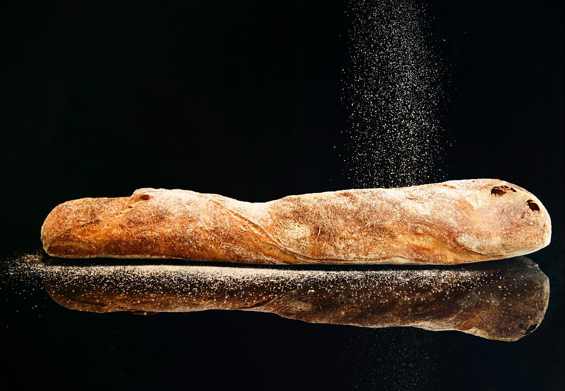 A baguette being sprinkled with flour