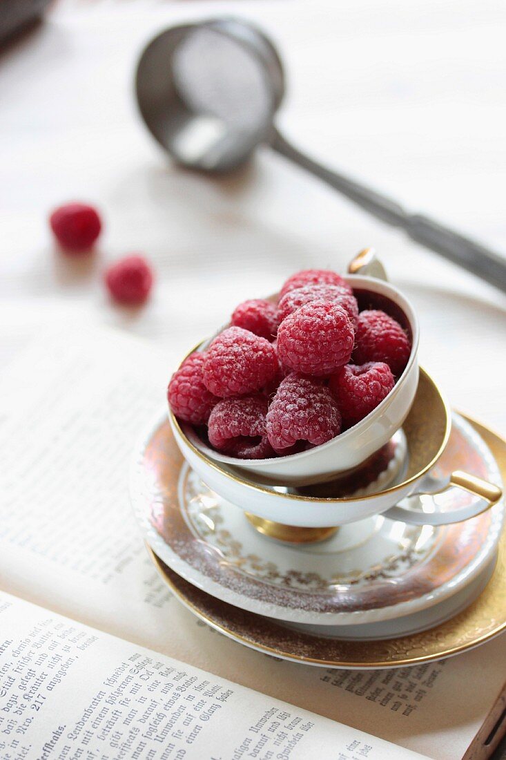Raspberries dusted with icing sugar in an old-fashioned teacup