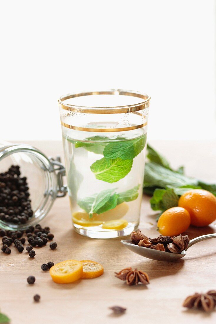 A glass of peppermint tea with mint leaves, a kumquat and spices