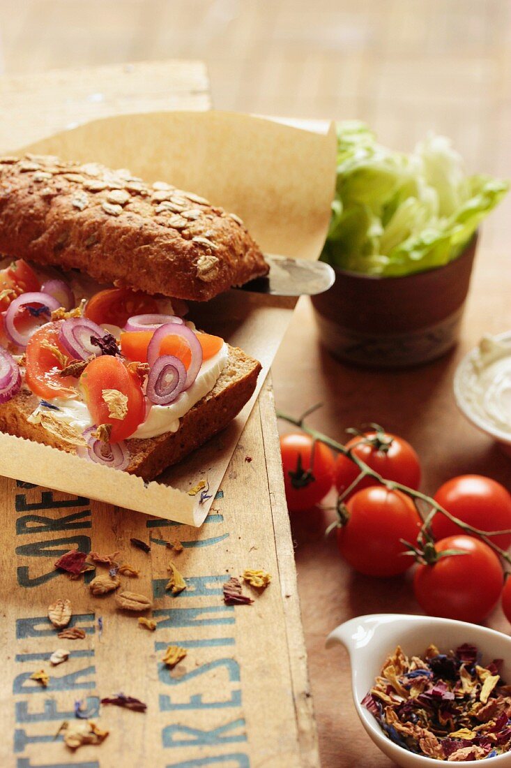 A slice of bread topped with cream cheese, tomatoes, onions and flowers