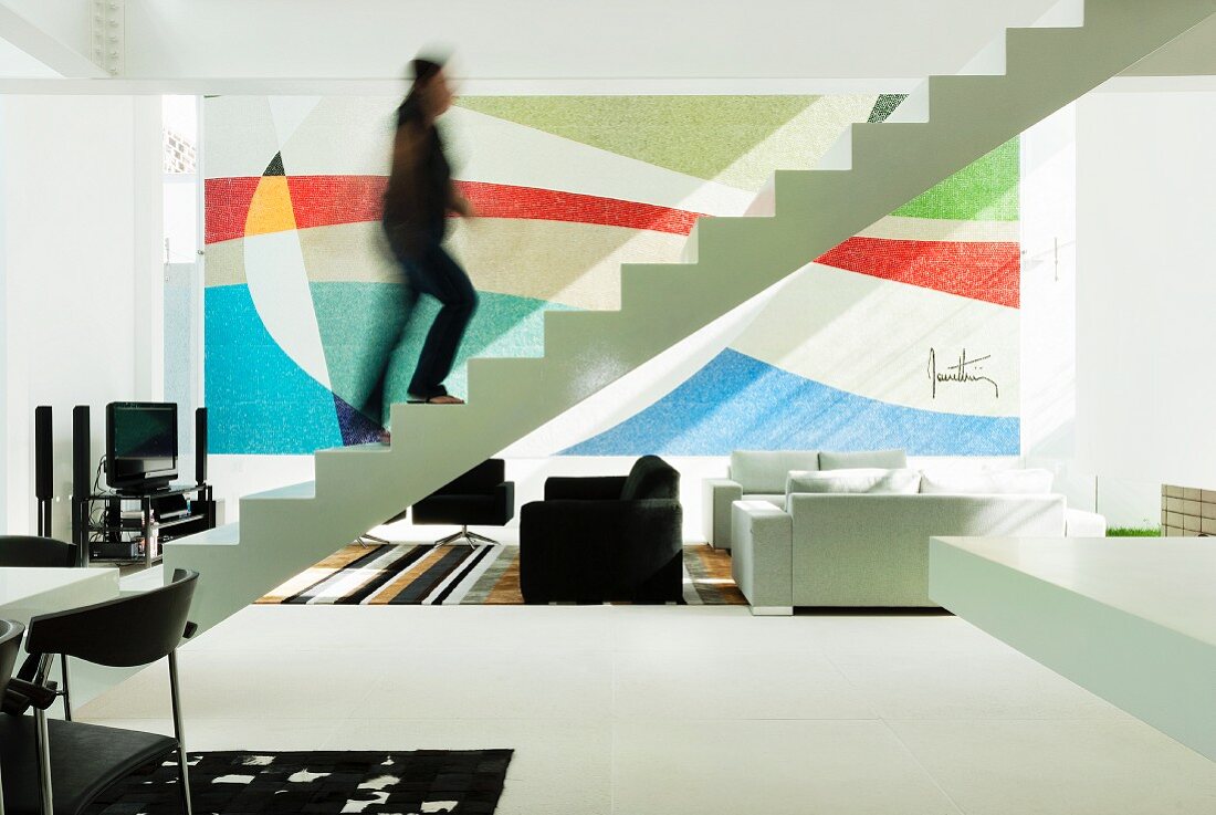 Woman, blurred by movement, walking up free-standing, zigzag staircase in open-plan, black and white interior with colourful artwork on wall
