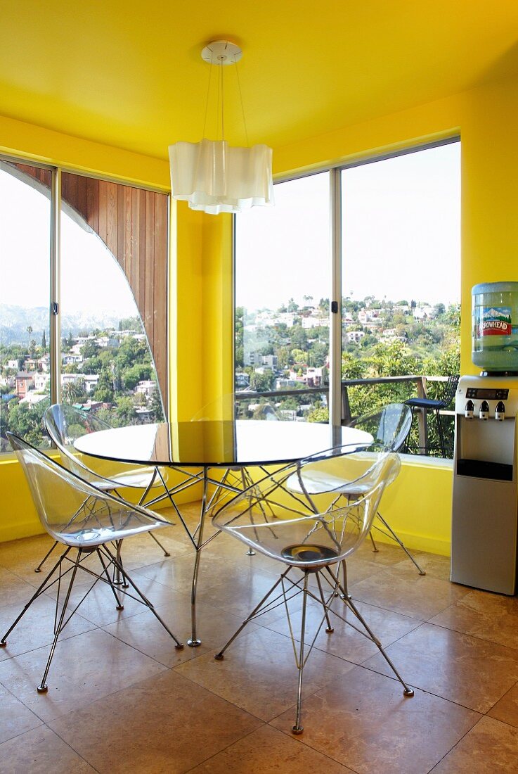 Classic, transparent, plastic shell chairs and round table in corner of yellow-painted room with panoramic windows