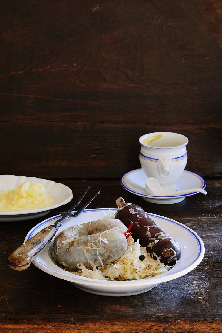 Black pudding and liver sausage with sauerkraut and mashed potatoes with a pot of mustard in the background