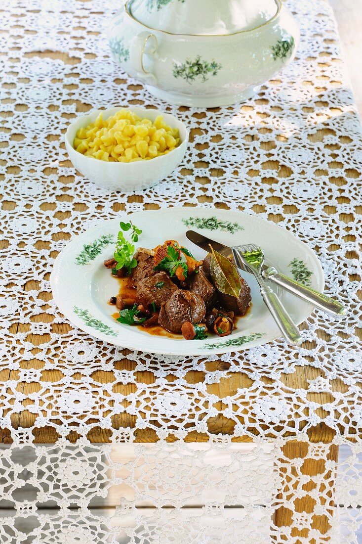 Venison goulash with mushrooms and Spätzle (soft egg noodles from Swabia) on a lace tablecloth