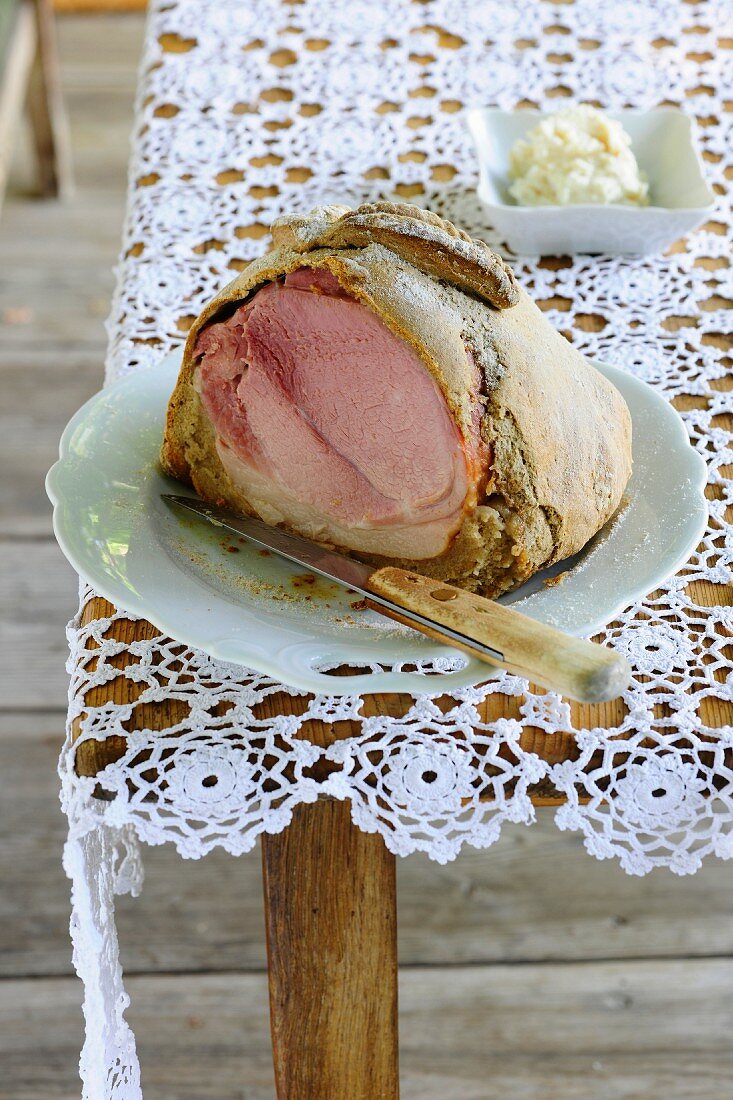 A sliced ham wrapped in bread served with creamy horseradish