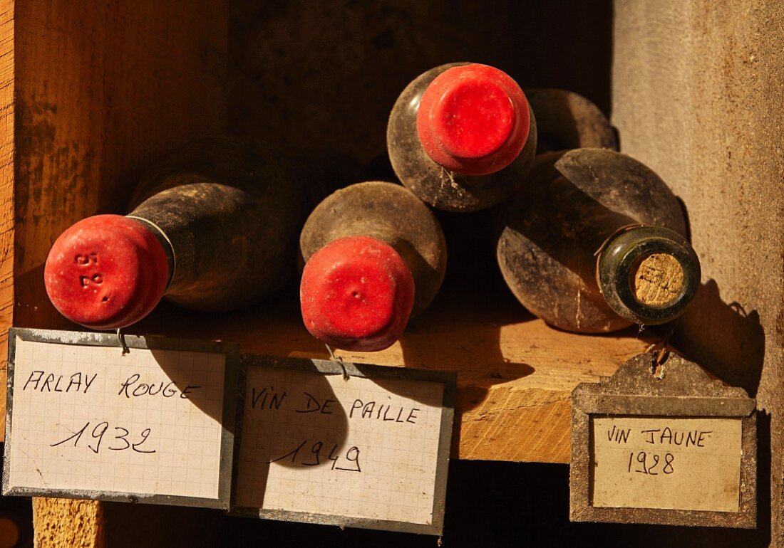 Vier staubige Weinflaschen in rustikalem Holzregal