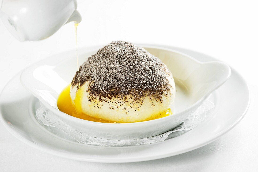 Melted butter being poured over a Germknödel (yeast dumpling filled with plum jam) topped with poppy seeds