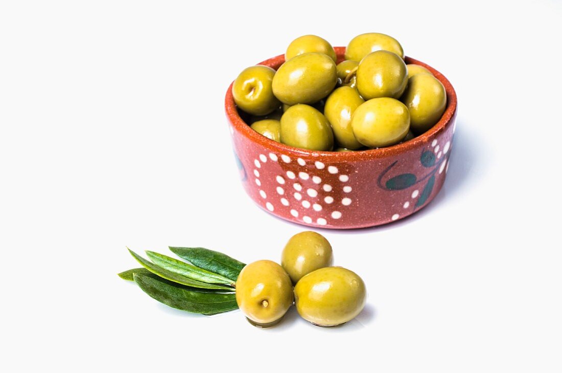 A bowl of green olives and some next to it