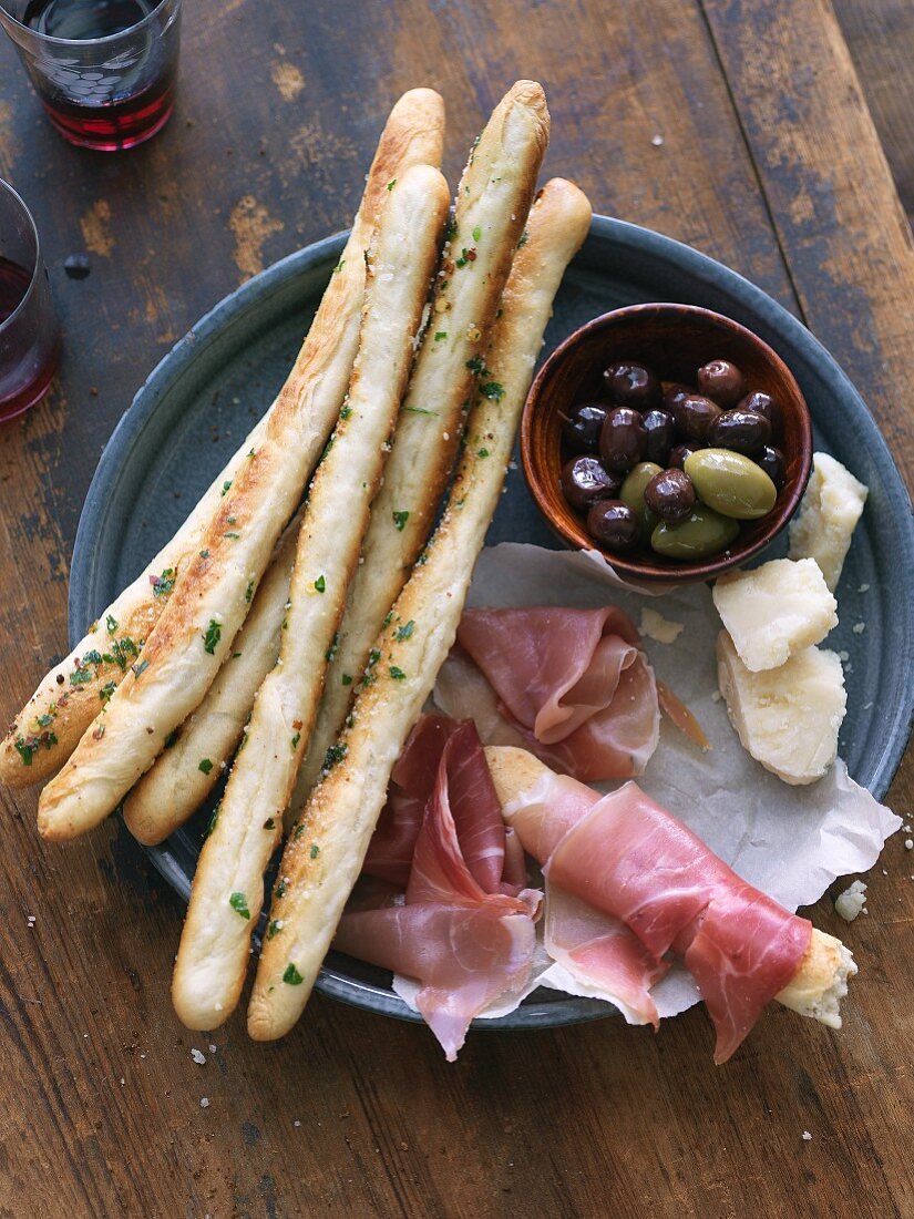 An appetiser platter with breadsticks, ham, cheese and olives