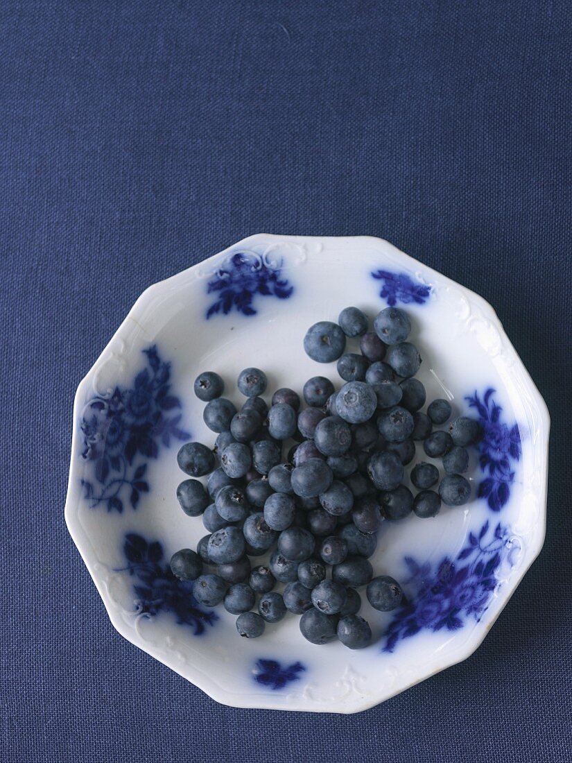 Blueberries on a plate on a blue surface