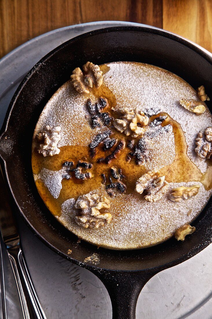 Pancake with walnuts and maple syrup in a pan (seen from above)