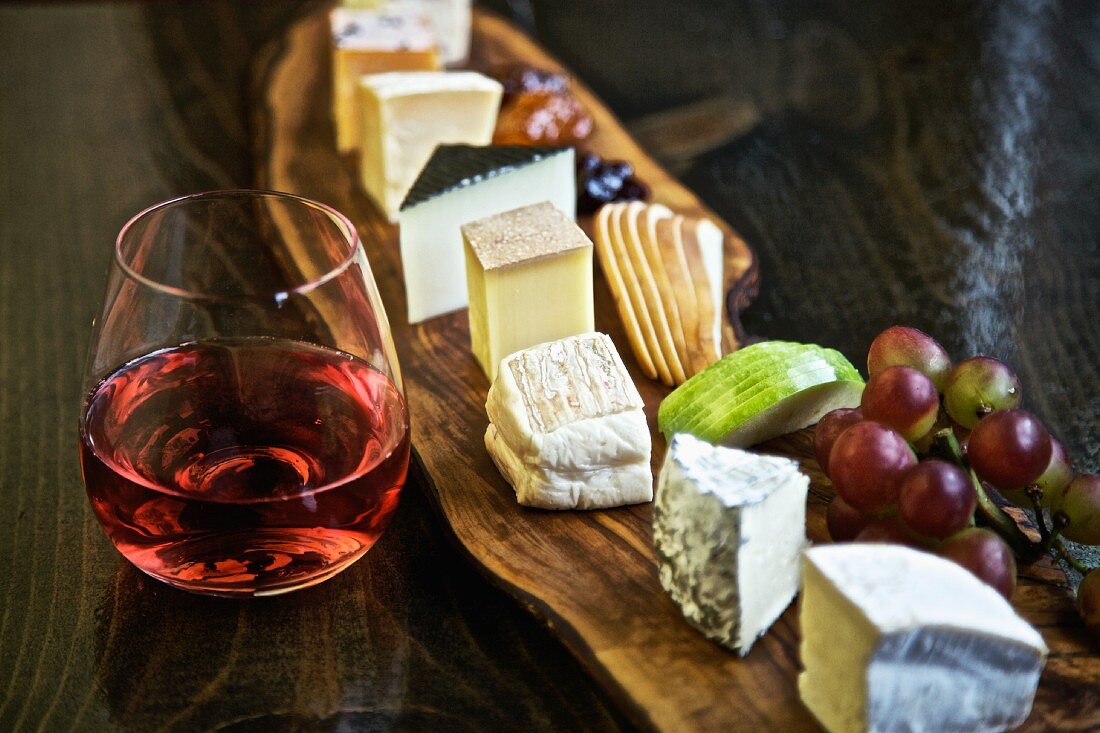 A mixed cheese platter with fruit and red wine
