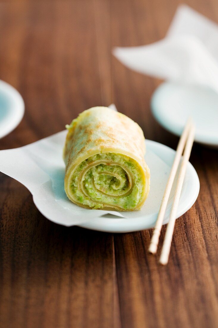 A stuffed pancake roll on a plate with chopsticks