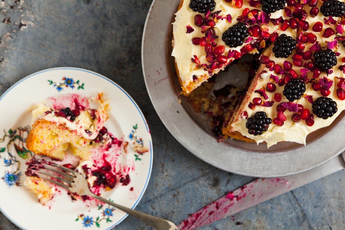 Biskuitkuchen mit Granatapfelkernen, Rosenblättern und Brombeeren (angeschnitten)