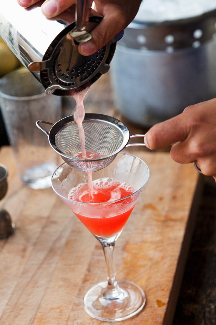 A cocktail being poured into a glass through a sieve