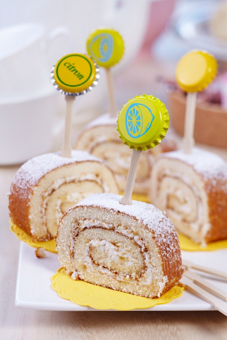 Slices of lemon Swiss roll decorated with toothpicks and bottle tops on white china plate