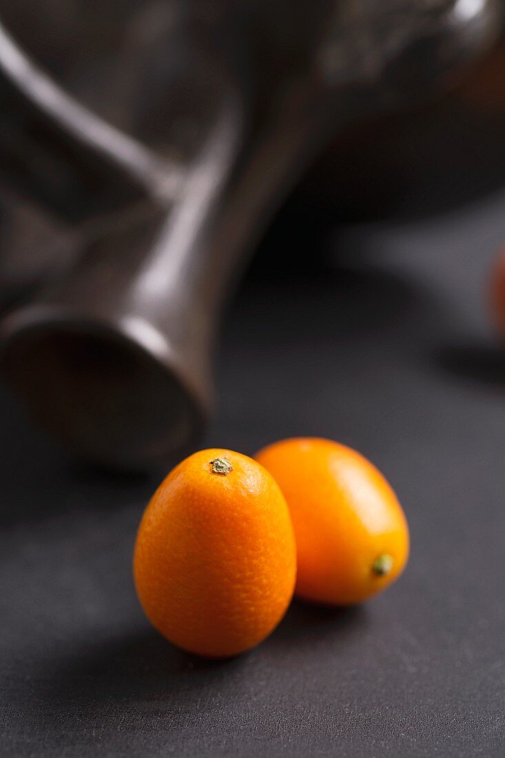 Two kumquats in front of a terracotta jug