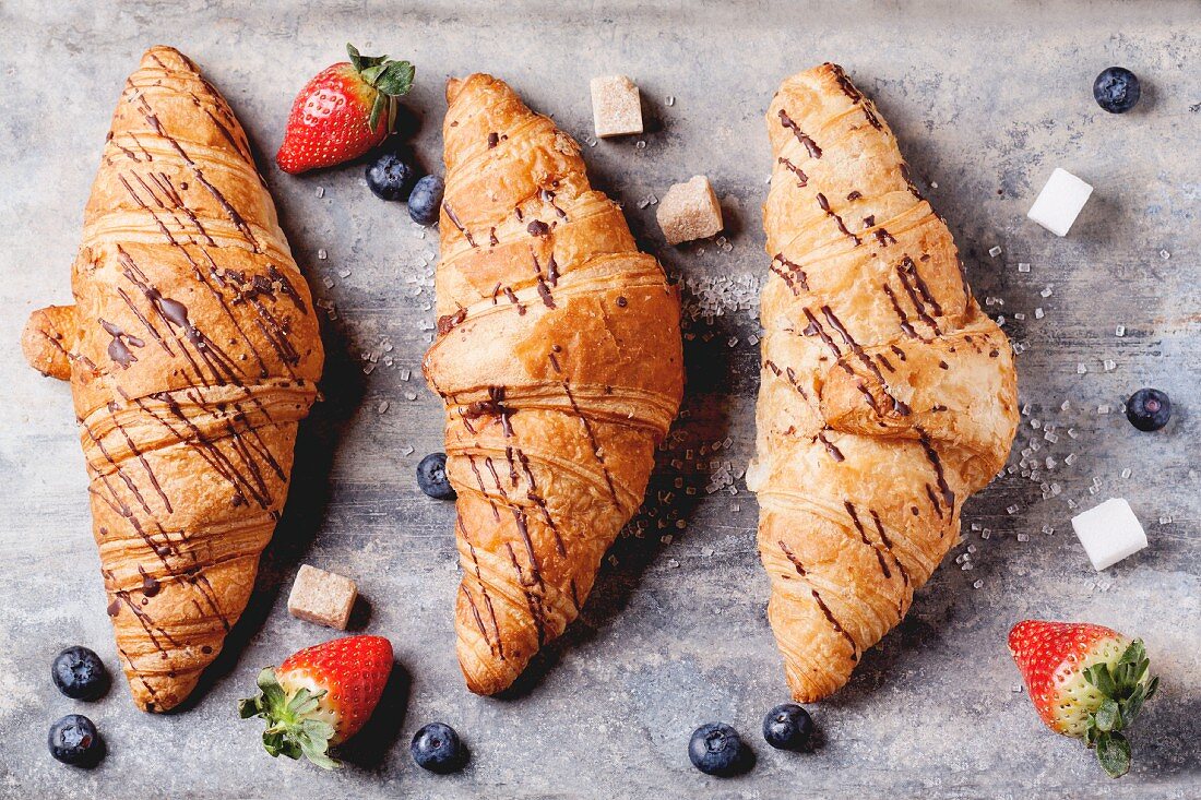 Drei Croissants mit Blaubeeren, Erdbeeren und Zuckerwürfeln