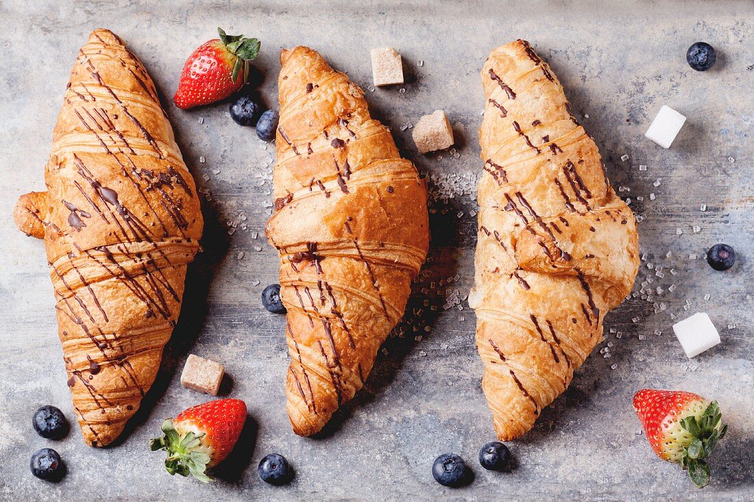 Three croissants with blueberries, strawberries and sugar cubes