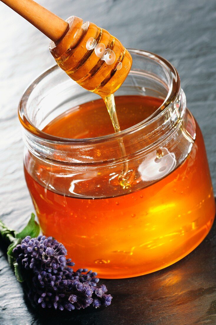 A jar of honey with a honey spoon and lavender flowers