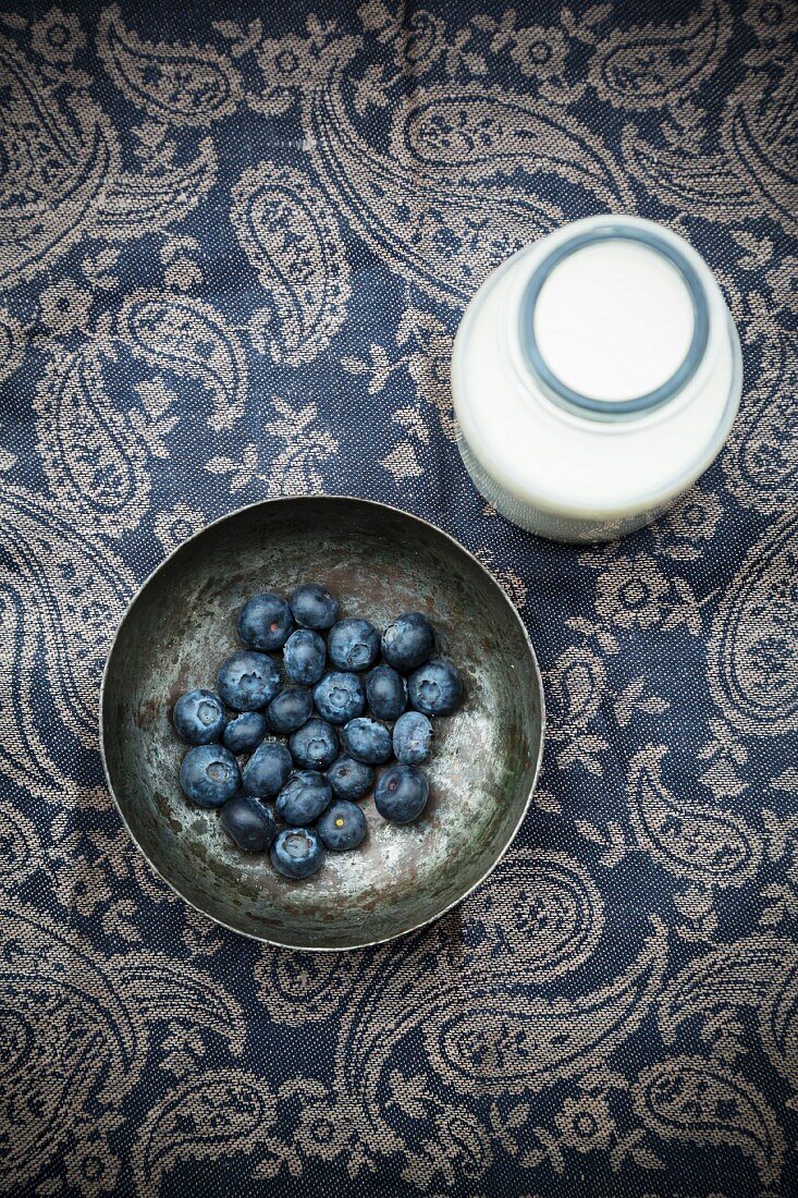Fresh blueberries in a metal bowl with a bottle of milk