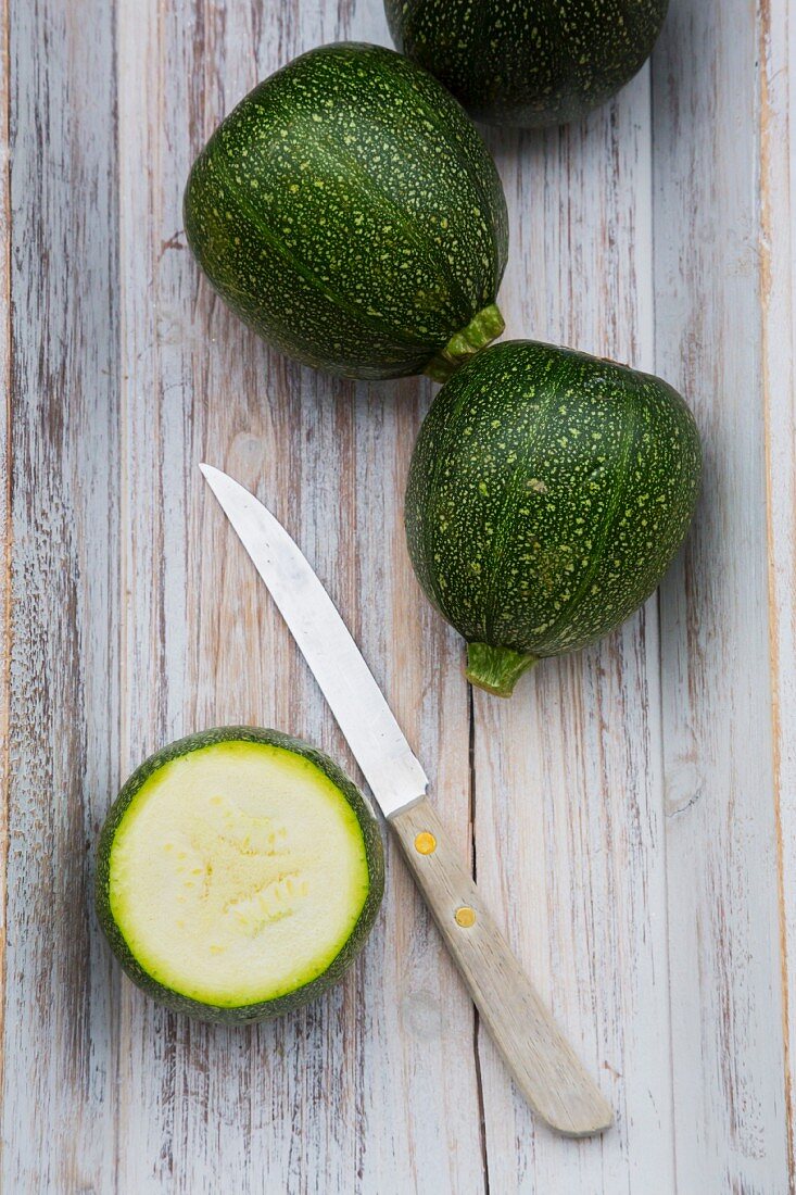 Round courgettes on a wooden tray with a knife