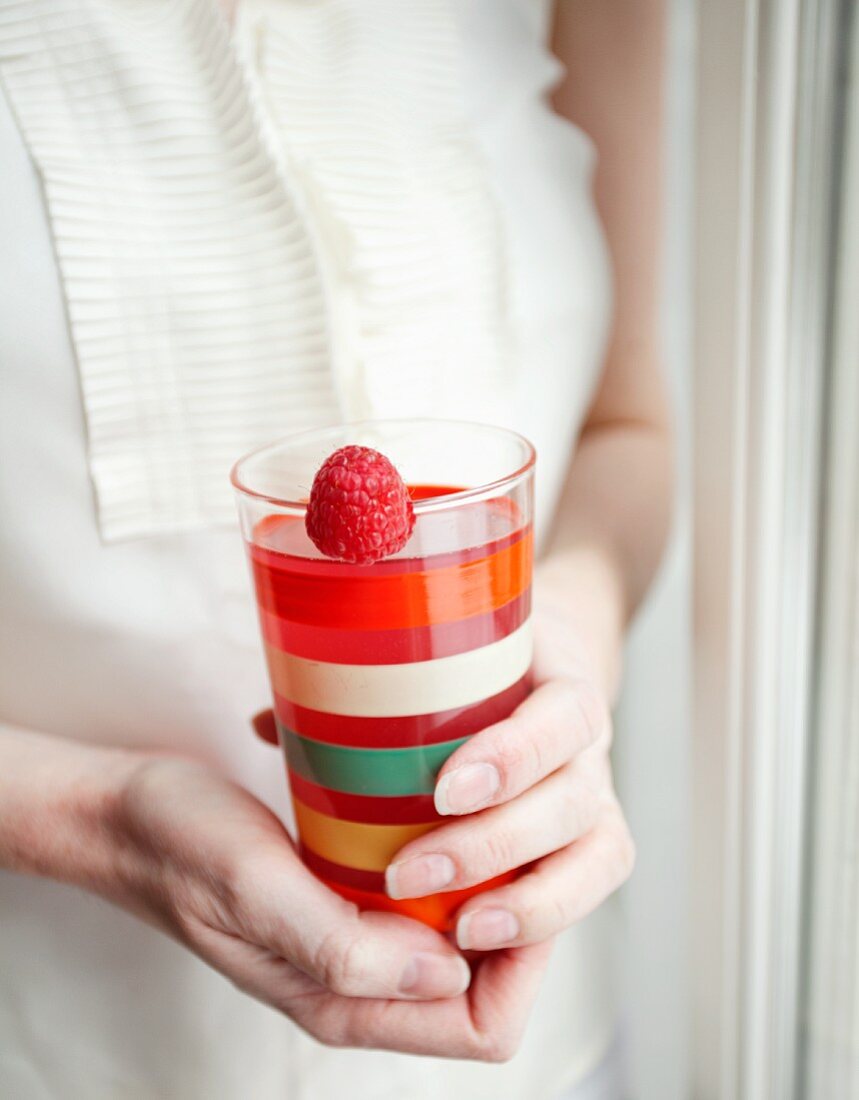A woman holding a glass of raspberry juice garnished with a fresh raspberry