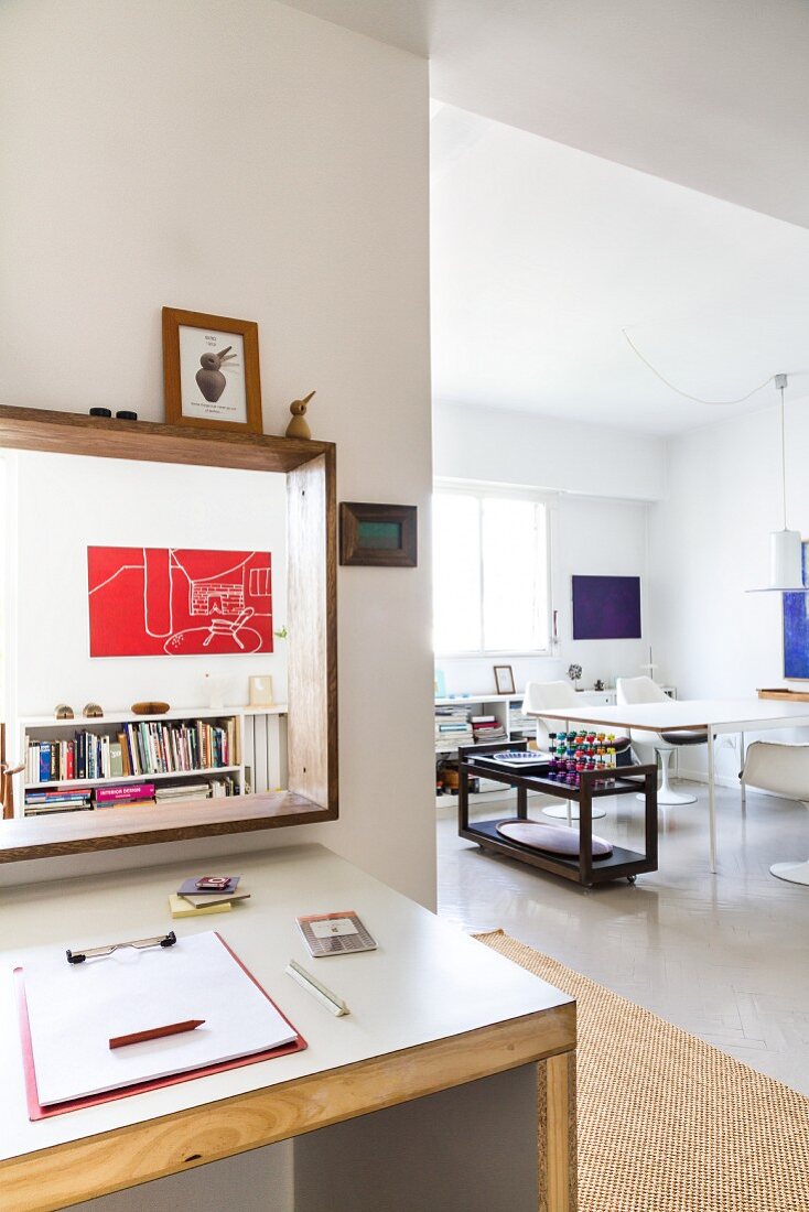 Corner of desk below hatch in wall with view of dining area to one side in open-plan interior