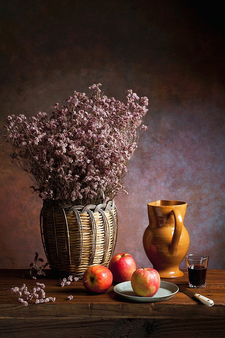 An arrangement featuring apples, dried flowers, an earthenware jug, wine and a knife