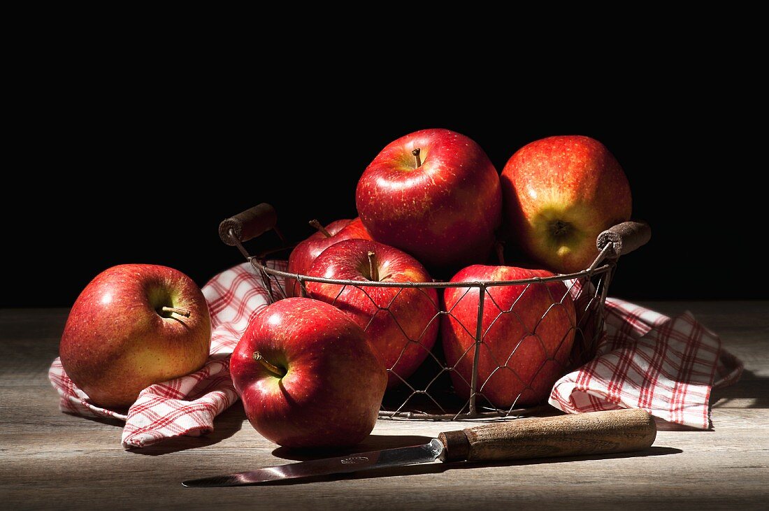 Äpfel im Drahtkorb mit karierter Serviette und Messer