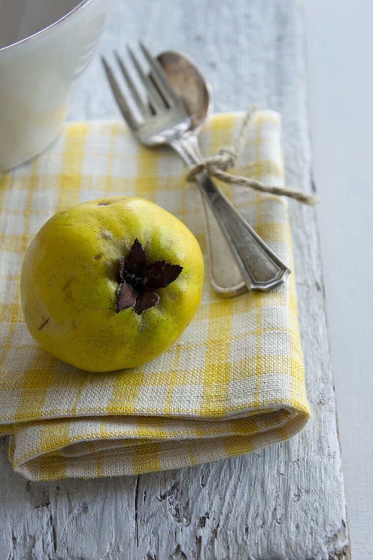 A quince and cutlery on a napkin