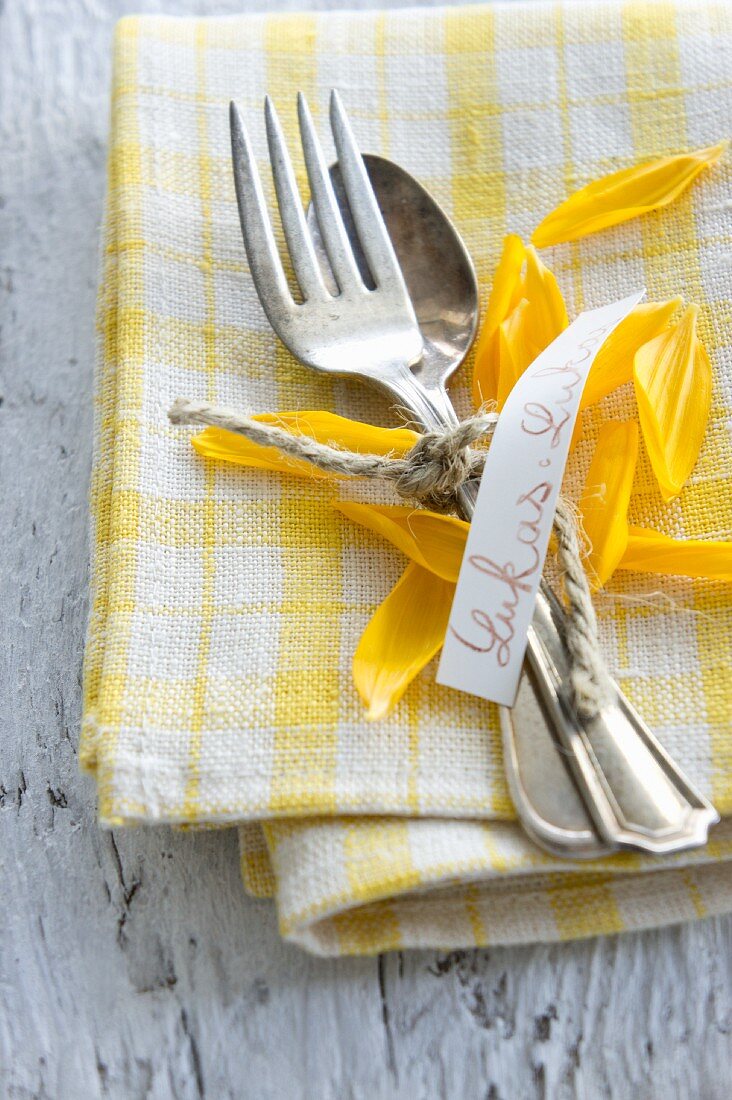 A place setting with a name tag and sunflower petals on a napkin
