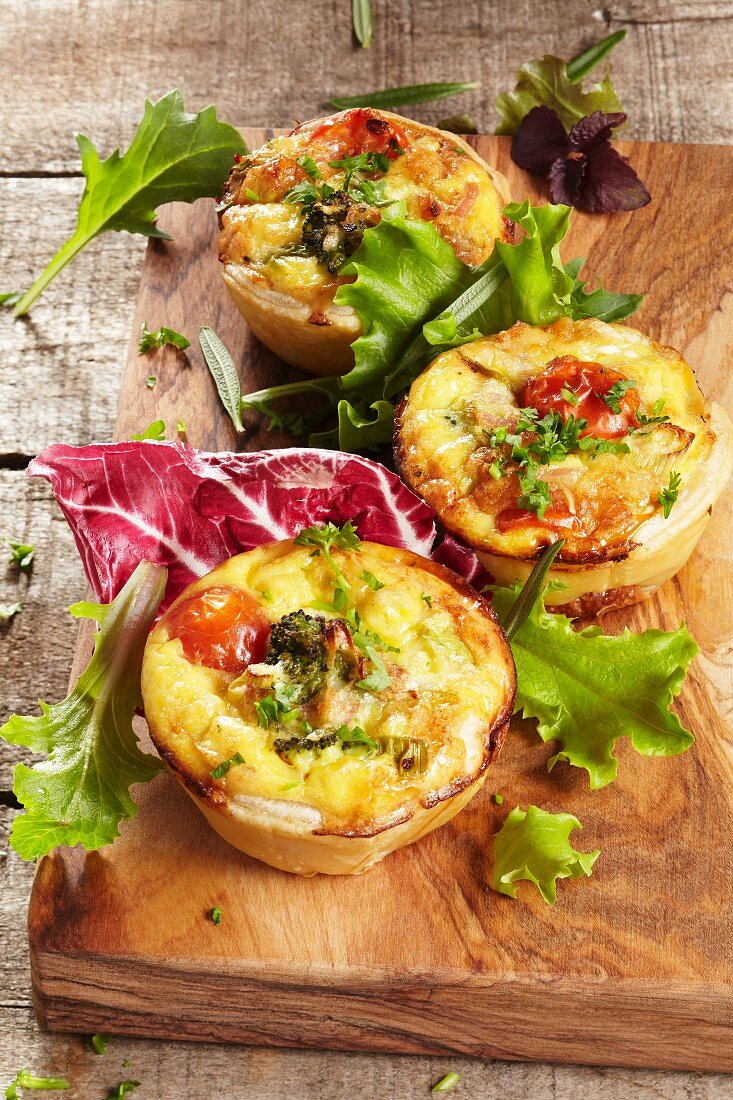 Three mini vegetable quiches with a salad garnish on a wooden board