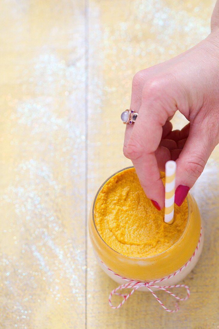 A hand placing a straw in a carrot and parsnip smoothie