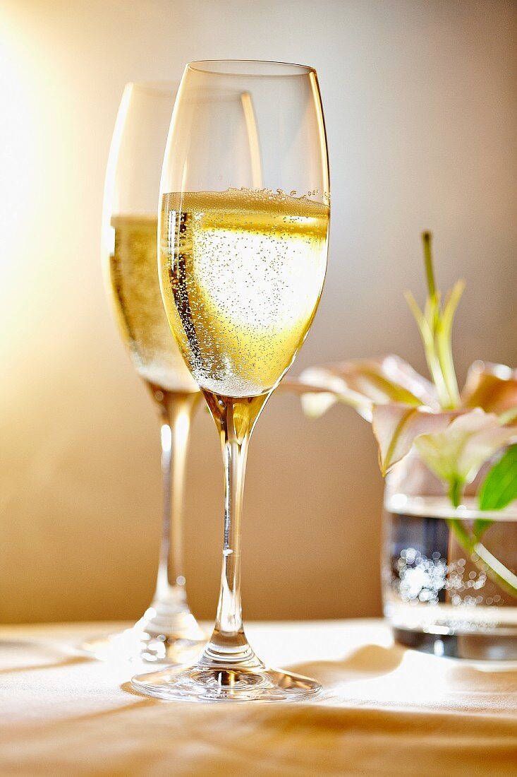 Two glasses of champagne in front of a vase of flowers