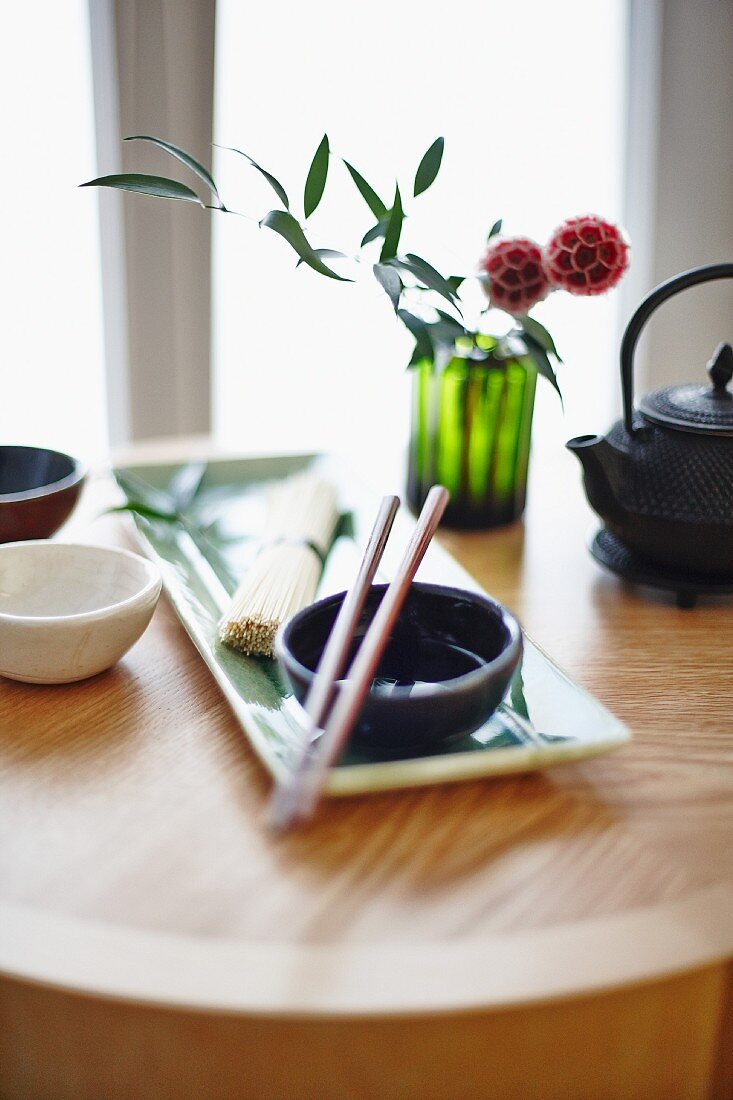 An oriental arrangement featuring a bowl, chopsticks, noodles and tea