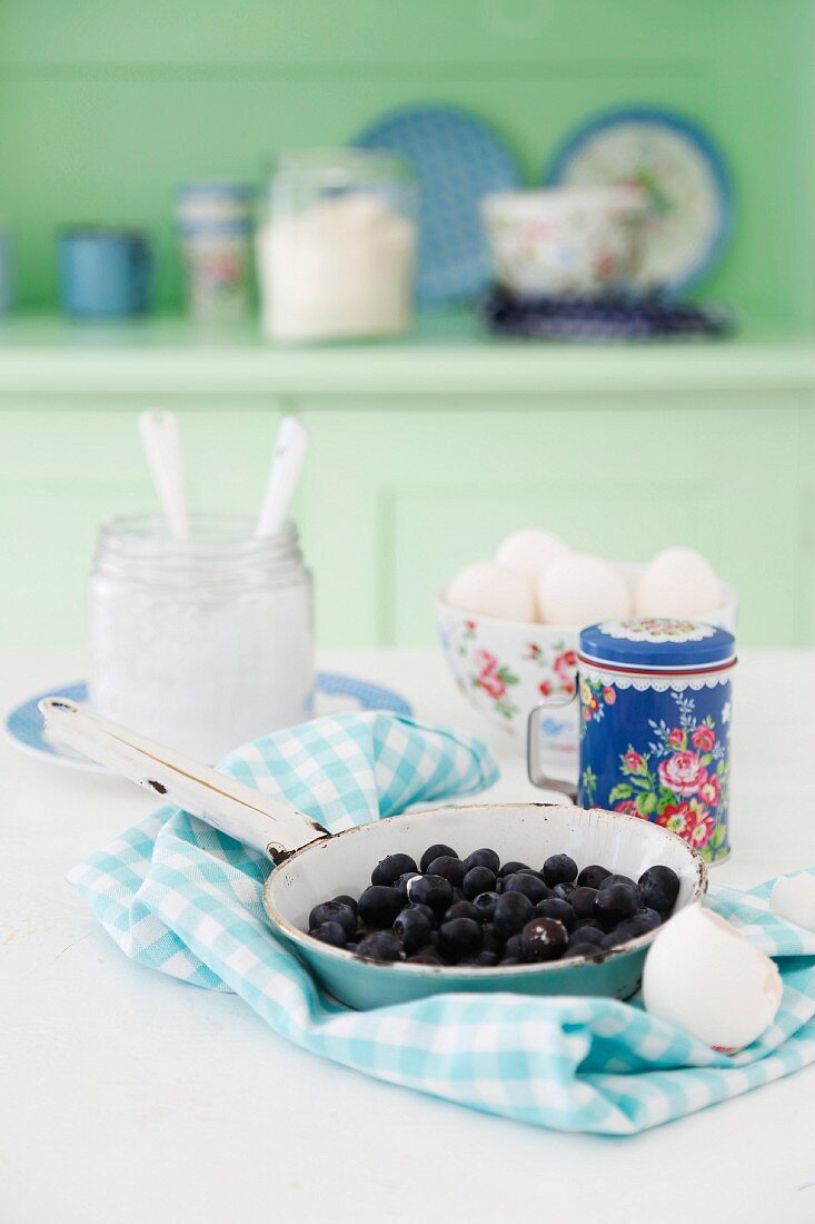 Blueberries in an enamel pan on a blue and white napkin with quark and eggs in the background