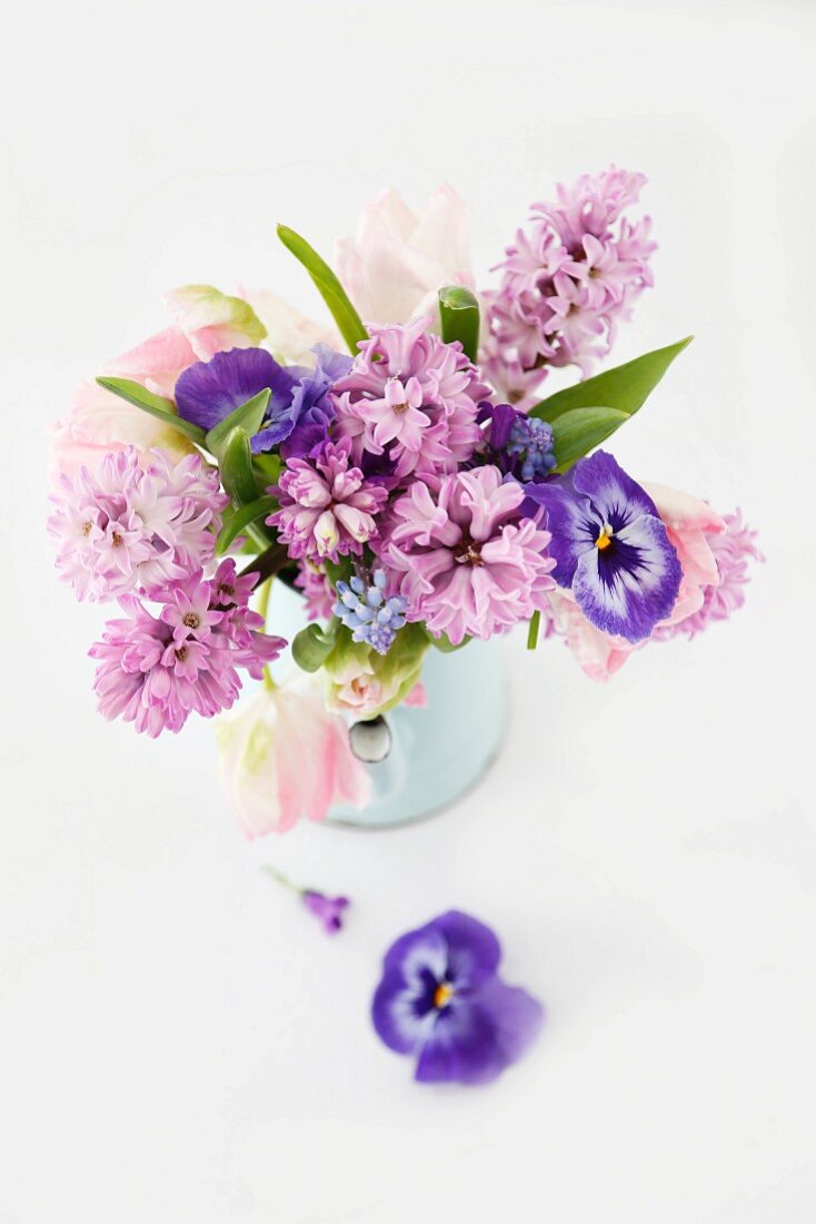 Spring posy of hyacinths, tulips and violas in pastel shades in pale blue enamel jug