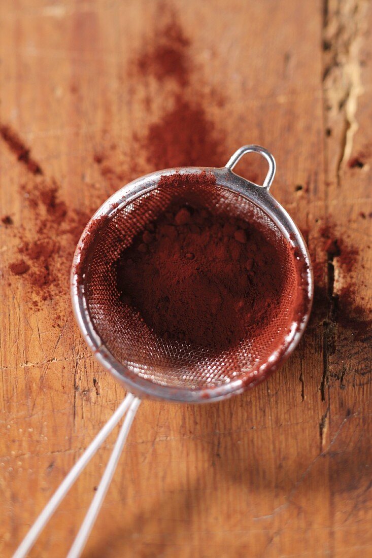 Cocoa powder in a sieve on wooden surface
