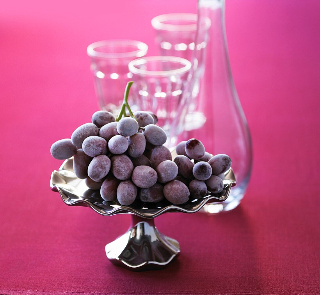Red grapes on a silver platter with an empty carafe and glasses in the background