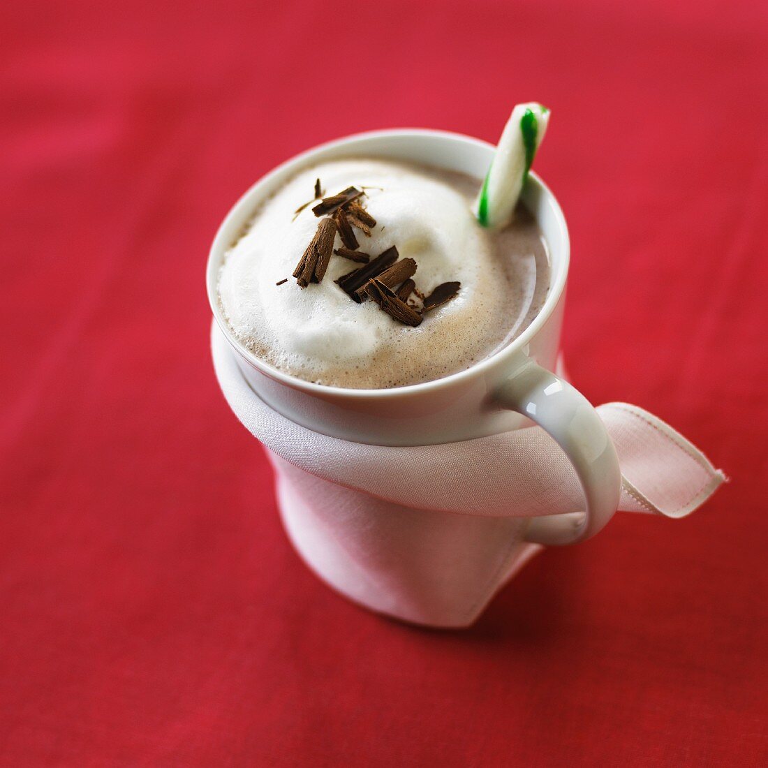 A mug of hot chocolate with milk foamy, grated chocolate and a candy cane
