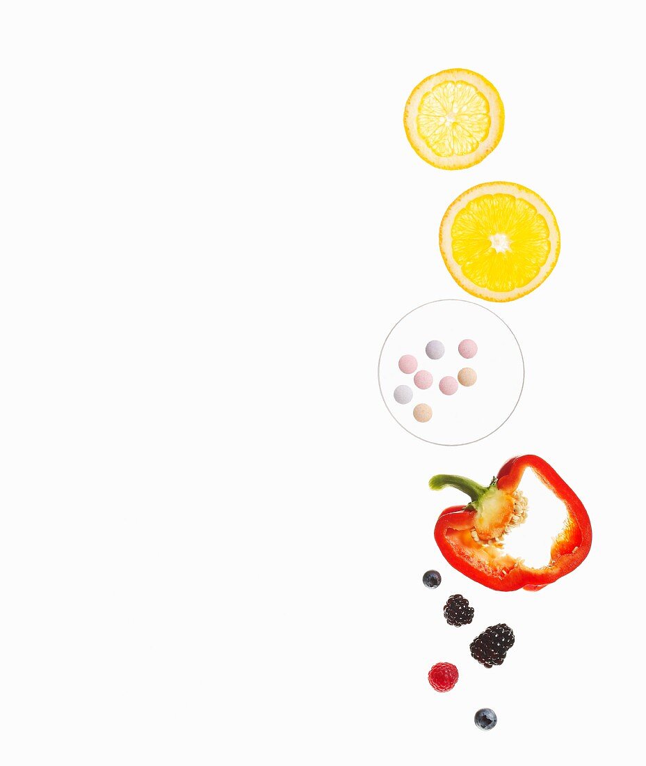 Slices of citrus fruits, pills, a red pepper and berries on a white surface