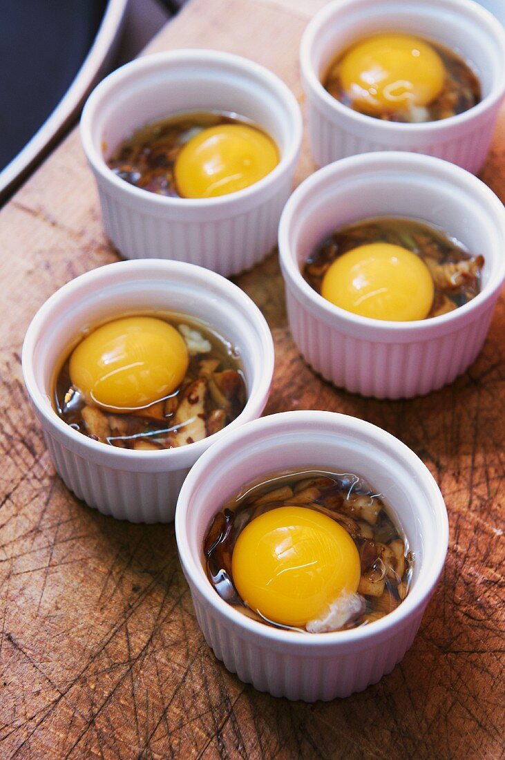 Oeuf Cocotte, raw eggs with mushrooms in oven-proof dishes ready to bake