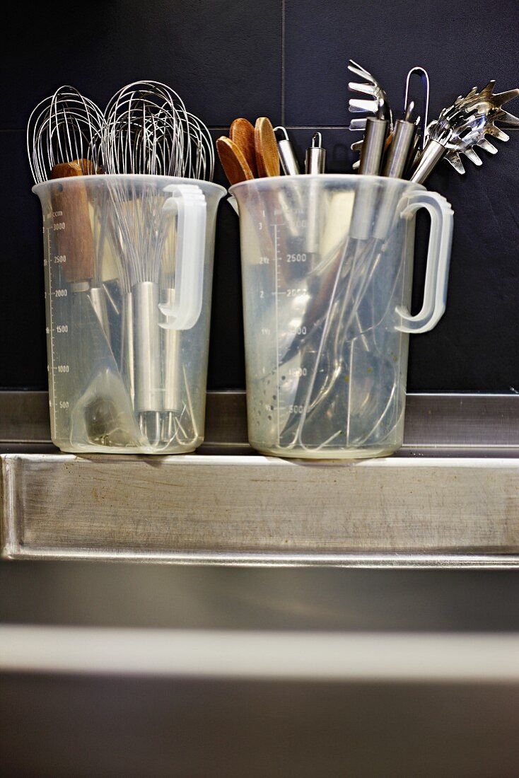 Two measuring jugs filled with kitchen utensils