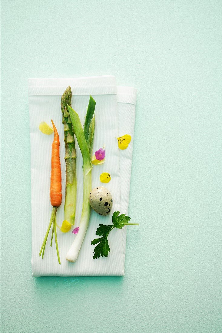 Spring vegetables with a quail's egg, parsley and edible flowers on a napkin