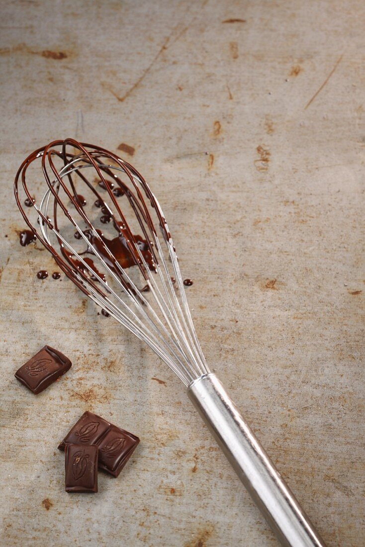 Pieces of chocolate and a whisk covered in melted chocolate