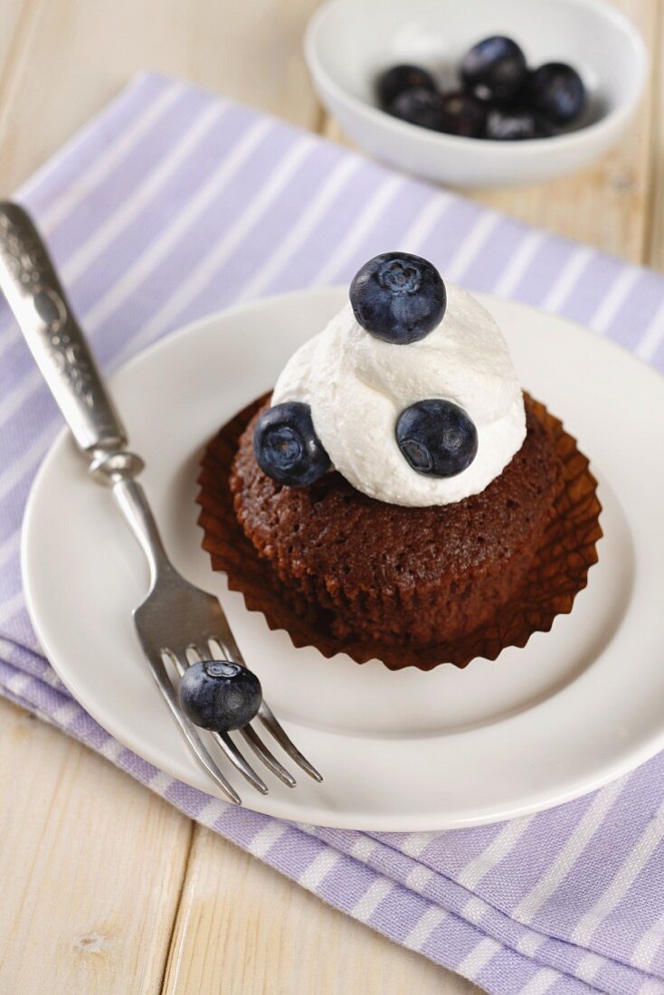 Chocolate muffin topped with cream and blueberries