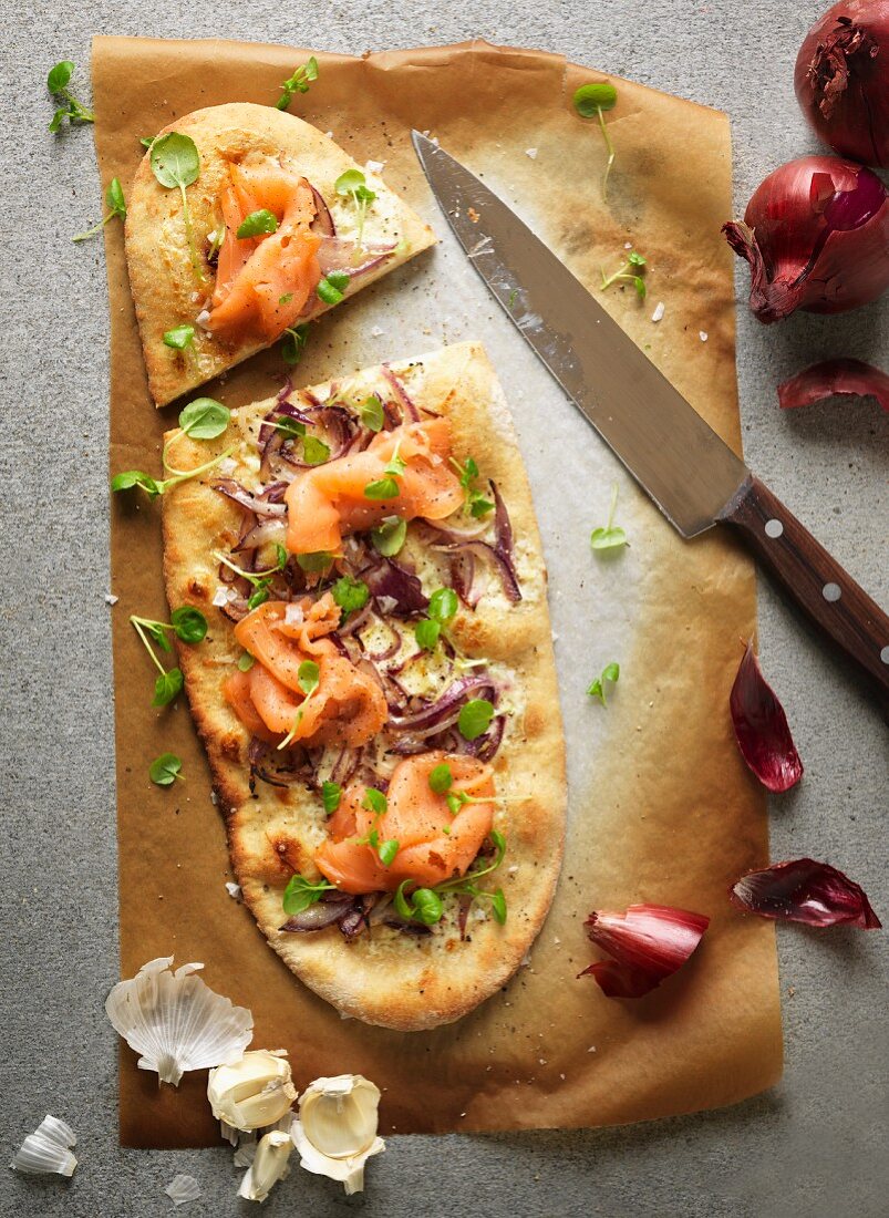 Pizza mit Sauerrahm und Knoblauch gebacken, belegt mit Räucherlachs, roten Zwiebeln und Brunnenkresse