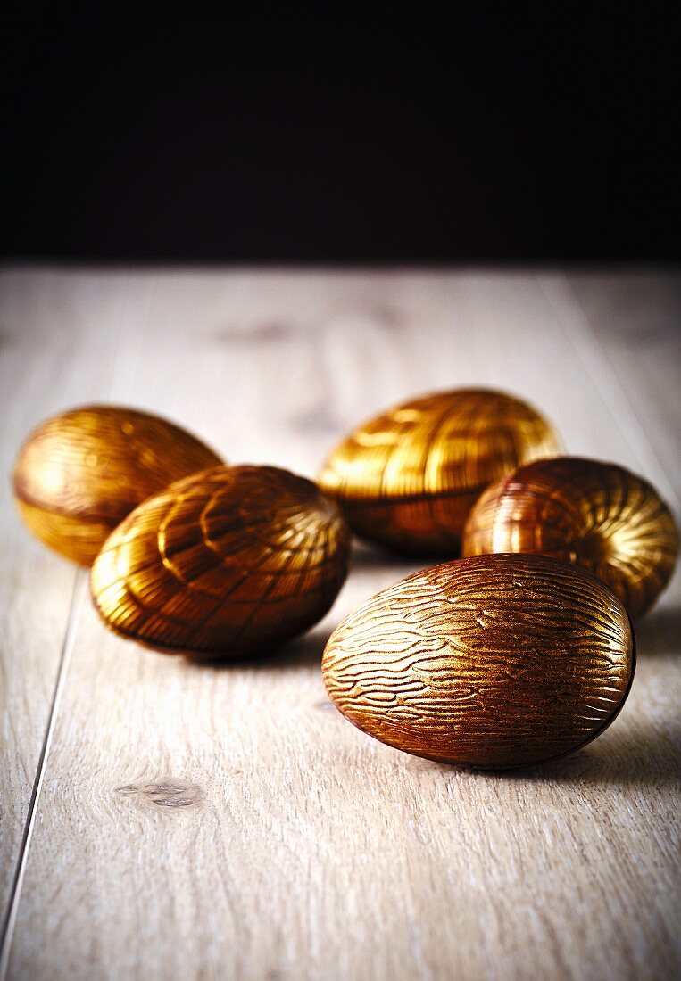 Mehrere goldene Schokoladenostereier auf Holzuntergrund