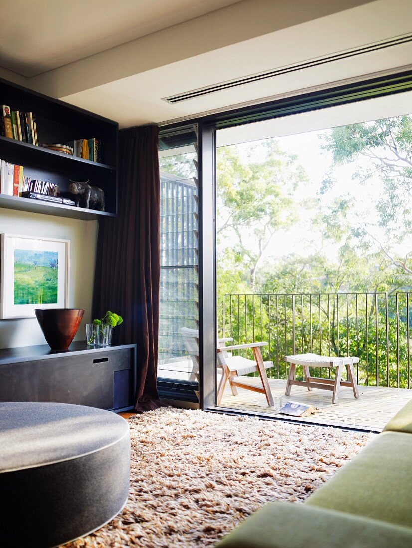 View from living room with long-pile rug onto balcony through wide-open glass sliding door